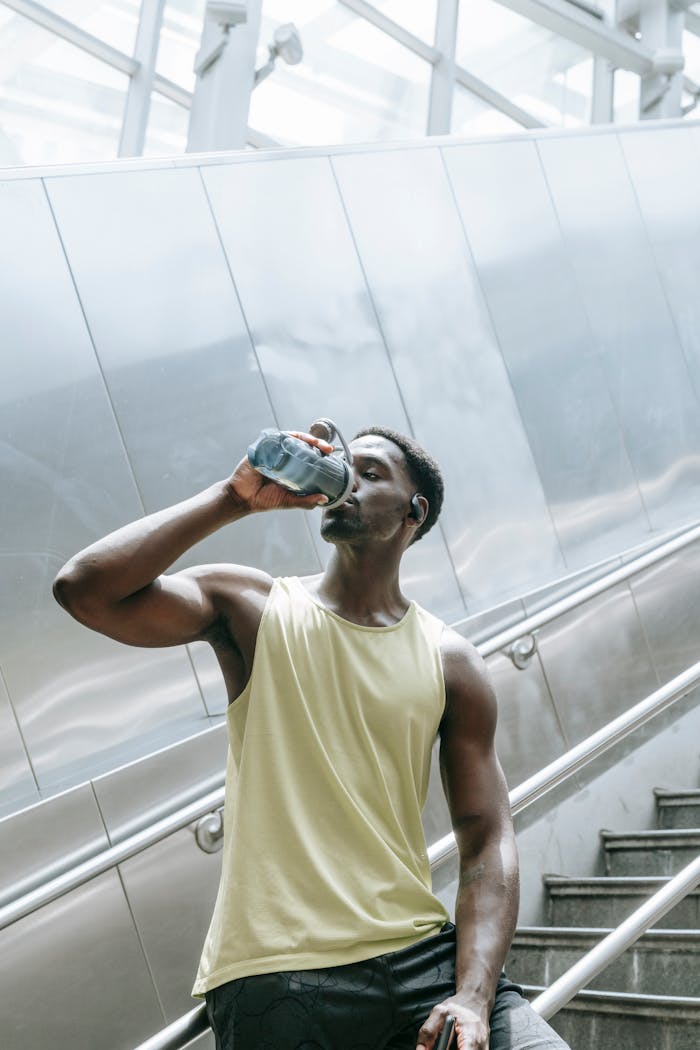 Fit young man hydrating with water bottle on city stairs